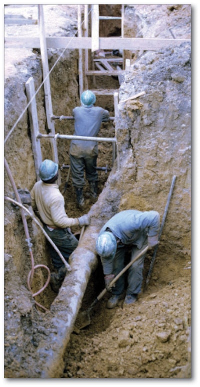 An example of a photo showing unsafe work practices on the eLCOSH site. The trench is partially unsupported, some of the shoring is not braced by screw jacks and there is a loose board above the workers’ heads.