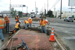Construction workers continue installation of a new median island that will prevent motorists from attempting to drive around lowered gate arms