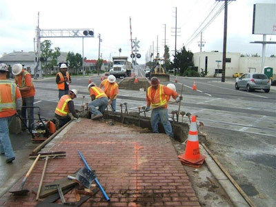 Construction workers continue installation of a new median island that will prevent motorists from attempting to drive around lowered gate arms