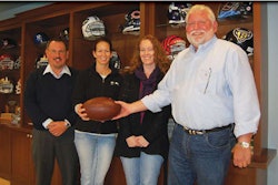 With helmets from their favorite teams – and favorite construction partners – in the background, Sports Construction Group president and CEO Paul Franks, right, hands the ball off to a trio of teammates, executive vice president George Pfeffer, vice president Julie Cipolla and controller Kelly Kost.
