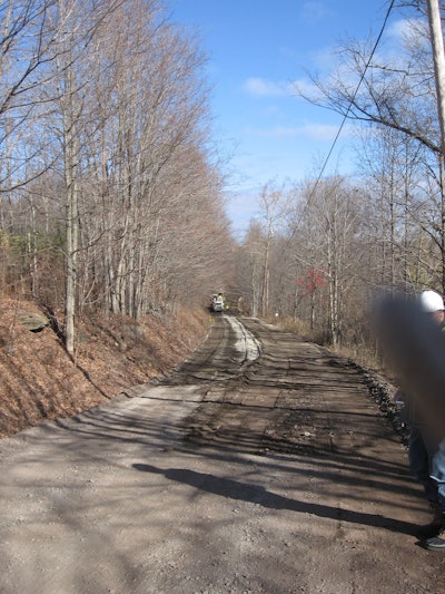 Background: Cement being mixed with the old road and base, with water being added through the reclaimer. Foreground: Reclaimed and compacted old road and base