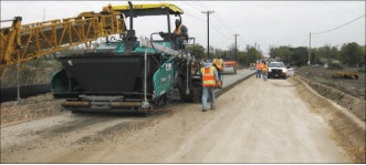 Reece Albert crew places roller compacted concrete on a haul road in New Braunfels, Texas. The contractor, working with CEMEX, placed the RCC pavement on a road that will carry heavy truck traffic. Photo depicts a GOMACO RTP-500 rubber-tracked placer, a Wirtgen/Vögele Super 2100-2 high density paver, and, in the distance, compaction equipment.