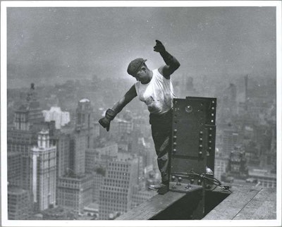 A workers signals to the hookman as the New York skyline sits peacefully below. Credit: Lewis Wickes Hine