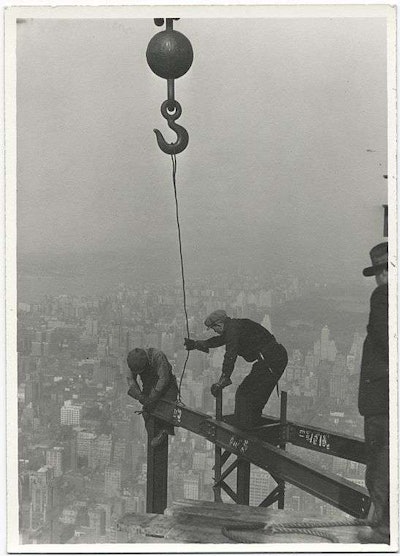 Two workers lower a beam into place with a crane. Credit: Lewis Wickes Hine