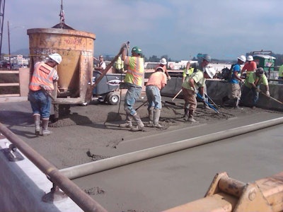 Crews smooth out concrete as a crane uses a bucket to pour the material. (Photo: WSDOT)