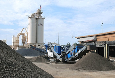 Raw RAP stockpile (foreground) is reduced to consistent sizes by a mobile impact crusher.