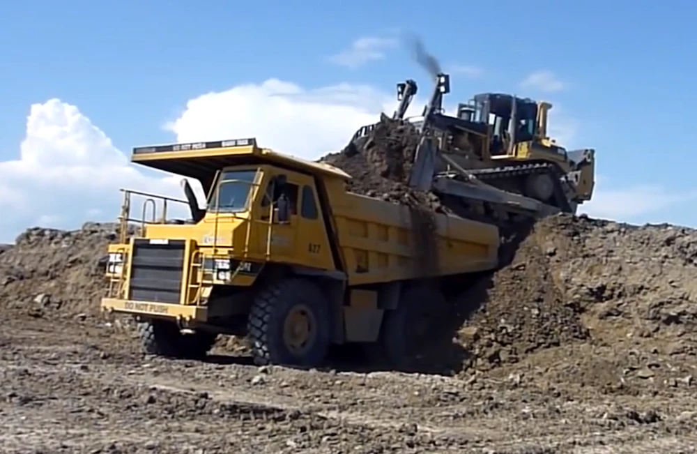Down an excavator, dozer operator loads rock truck by driving on top of ...