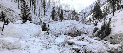 An ITD worker (in orange) stands where road should be. An estimated eight avalanches have occurred in the past few days on Highway 21 in Idaho, completely covering a 12-mile portion of the road. (Photo Credit: ITD, via Boise State Public Radio)