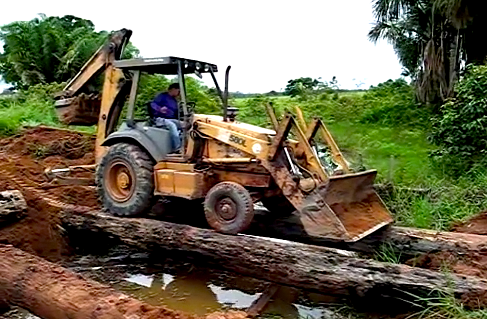 Backhoe crosses water on bridge made of logs