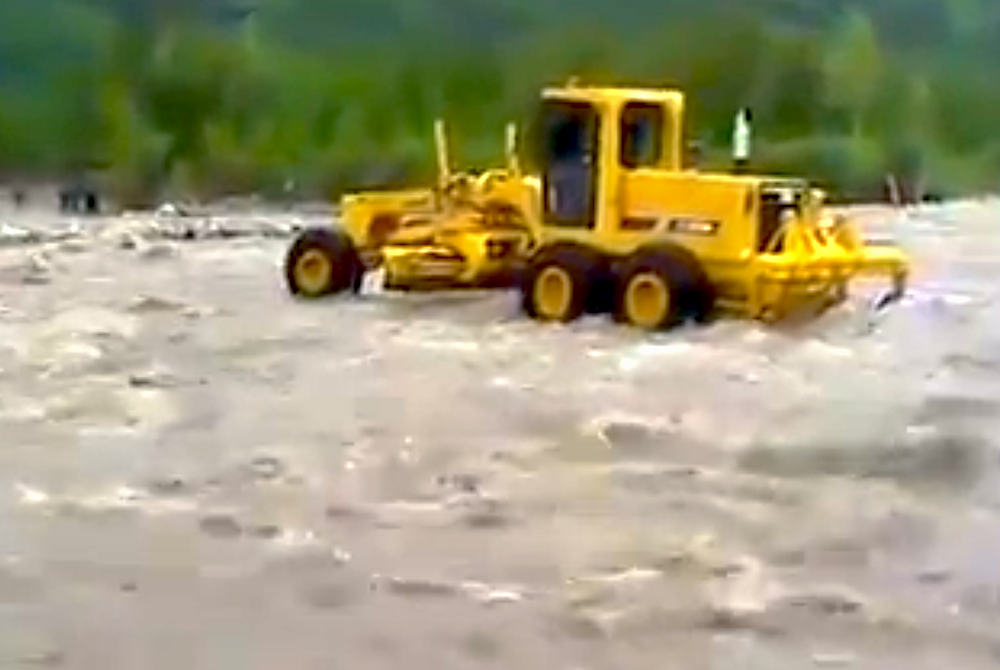 Motor grader swept down river