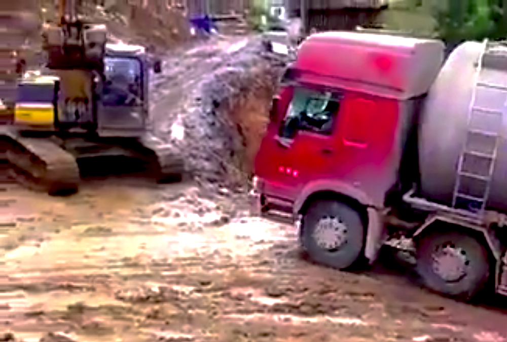 Excavator pulls truck up hill