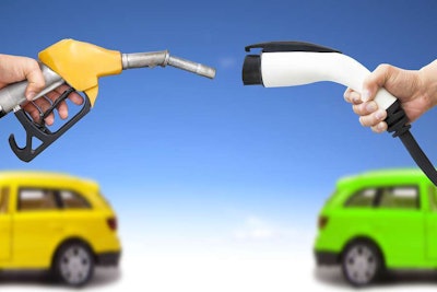 Electric Car And Gasoline Car Concept. Hand Holding Gas Pump And