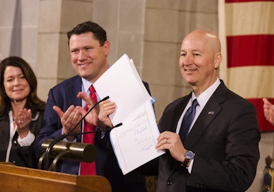 Gov. Pete Ricketts holds up LB 339 while Director Kyle Schneweis, background, and others applaud during Thursday’s press conference at the Capitol. Photo: Jake Daniels