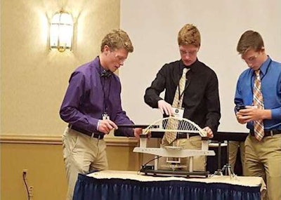 Negaunee High School students (left to right) Thomas Ziegler, Zach Champion and Mitch LaBelle test their bridge, which won the 11-12th grade division at the 15th Annual TRAC Bridge Challenge this week. The Negaunee team’s bridge held 254 pounds, while weighing in at just 26 grams, for a strength-to-weight ratio of 4,440.4-to-1. (Michigan DOT)