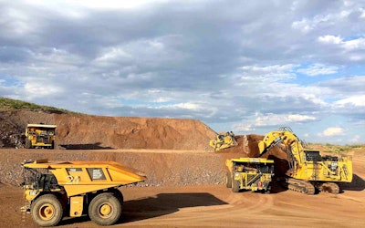 A Komatsu 930E positioned in the top left background during a Caterpillar autonomous mine truck demonstration.