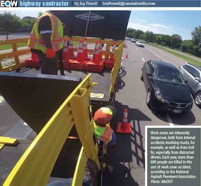 Two workers wearing safety vests on a truck in a work zone while traffic continues