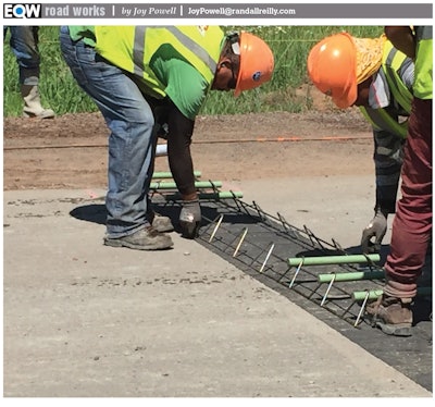 Road workers laying nonwoven geotextile fabric across road