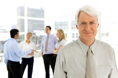 Businessmen and businesswomen talking together while one older businessman stands to the side