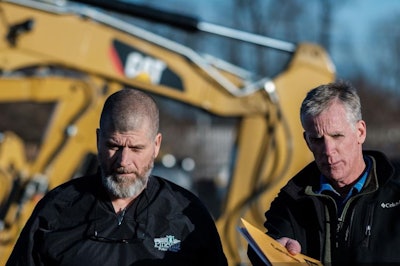 Two men in front of Caterpillar heavy duty equipment