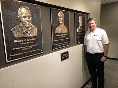 Gary Bridwell carries on the legacy of Ditch Witch customer service and growth, now owning the company’s first dealership. From left, plaques in the Oklahoma City dealership commemorate the dealership’s founder, Russell Sadler; Ditch Witch founder Ed Malzahn; and Gary’s father, John Bridwell.