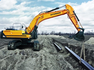 Hyundai excavator lowering a pipe into a trench