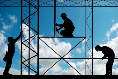 Silhouette of construction workers and metalwork against a blue sky with fluffy white clouds