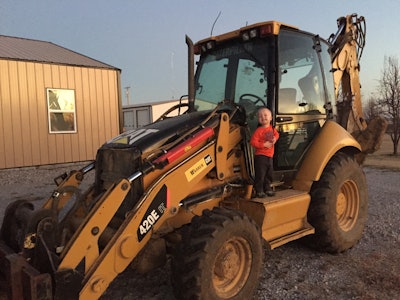 Bret Barnhart's son, Cole Barnhart, standing on CAT 420E loader backhoe