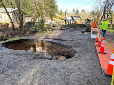 Sinkhole in road with Bailey Bridge assembly in the background