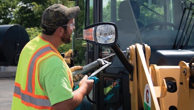 Equipment service technician greasing joints on a piece of heavy equipment
