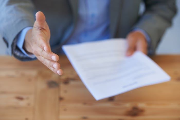Person extending hand to shake while holding paperwork