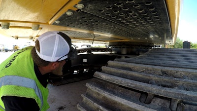 A man inspecting the undercarriage of a piece of heavy construction equipment