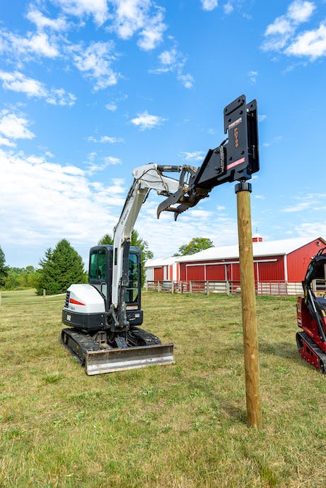 compact excavator with post driver attachment in operation