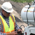 A man wearing a safety vest and hard hat looking at his cell phone