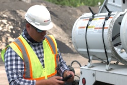 A man wearing a safety vest and hard hat looking at his cell phone