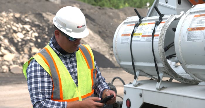 A man wearing a safety vest and hard hat looking at his cell phone