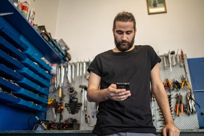 A person in a black shirt texting while standing in front of a wall of tools