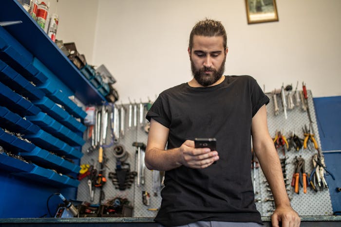 A person in a black shirt texting while standing in front of a wall of tools