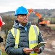 Construction supervisor holding a tablet and talking to an employee.
