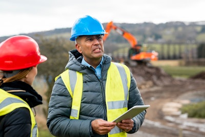 Construction supervisor holding a tablet and talking to an employee.