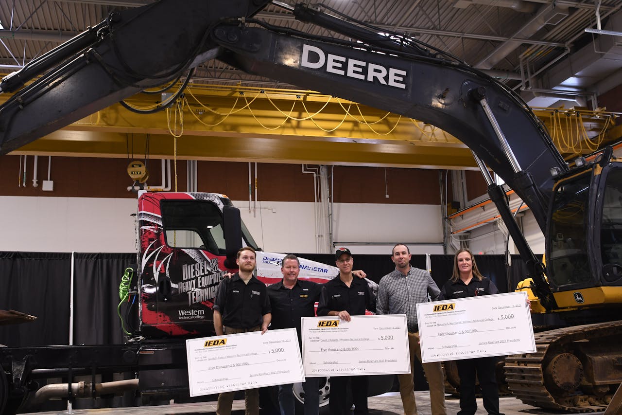 Students standing in front of Deere excavator to accept a scholarship check.