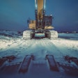 Excavator at snowy construction site at dusk.