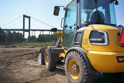 Volvo L25 electric wheel loader parked at urban jobsite near a bridge.