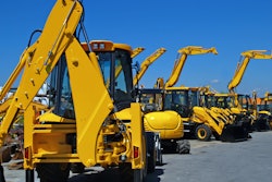 Construction equipment parked in a row in an industrial lot.