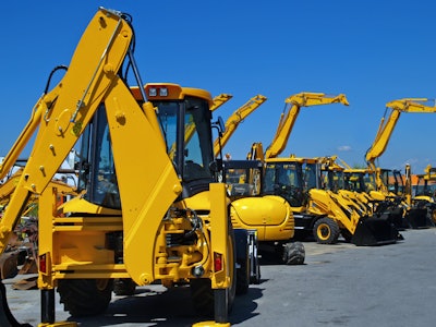 Construction equipment parked in a row in an industrial lot.