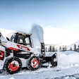Bobcat skid steer with snow blower attachment clearing a road.