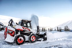 Bobcat skid steer with snow blower attachment clearing a road.