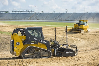 John Deere CTL with grader blade attachment and bulldozer at a construction site.