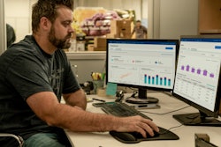 Man sitting at a desk looking at two computer monitors that are displaying Ford Pro E-Telematics graphs