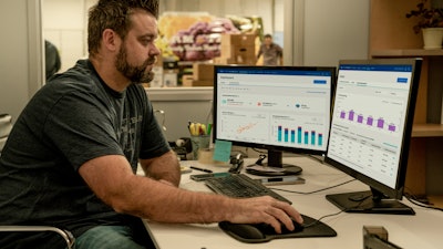 Man sitting at a desk looking at two computer monitors that are displaying Ford Pro E-Telematics graphs