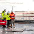 Three construction workers standing on a roof looking at plans.